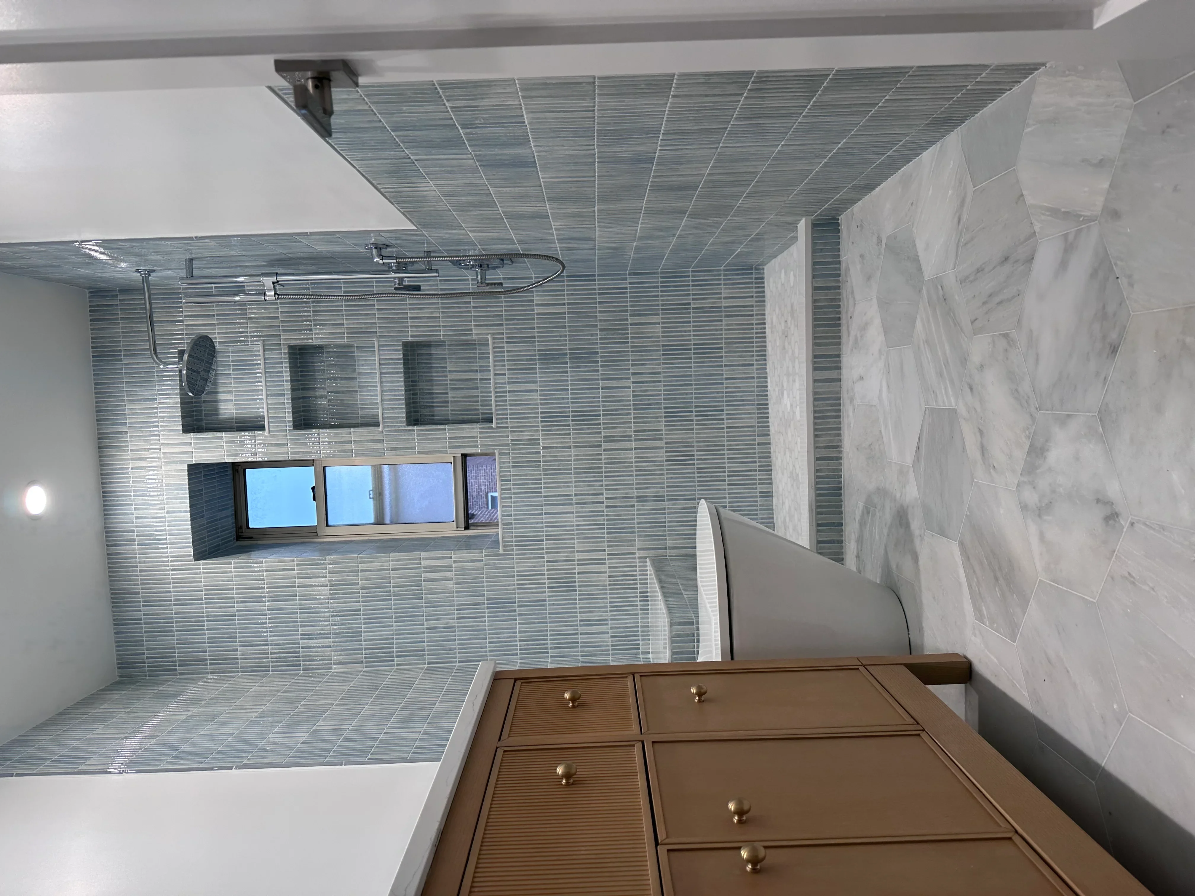 Modern bathroom with frameless glass shower, linear tile walls, and marble accents