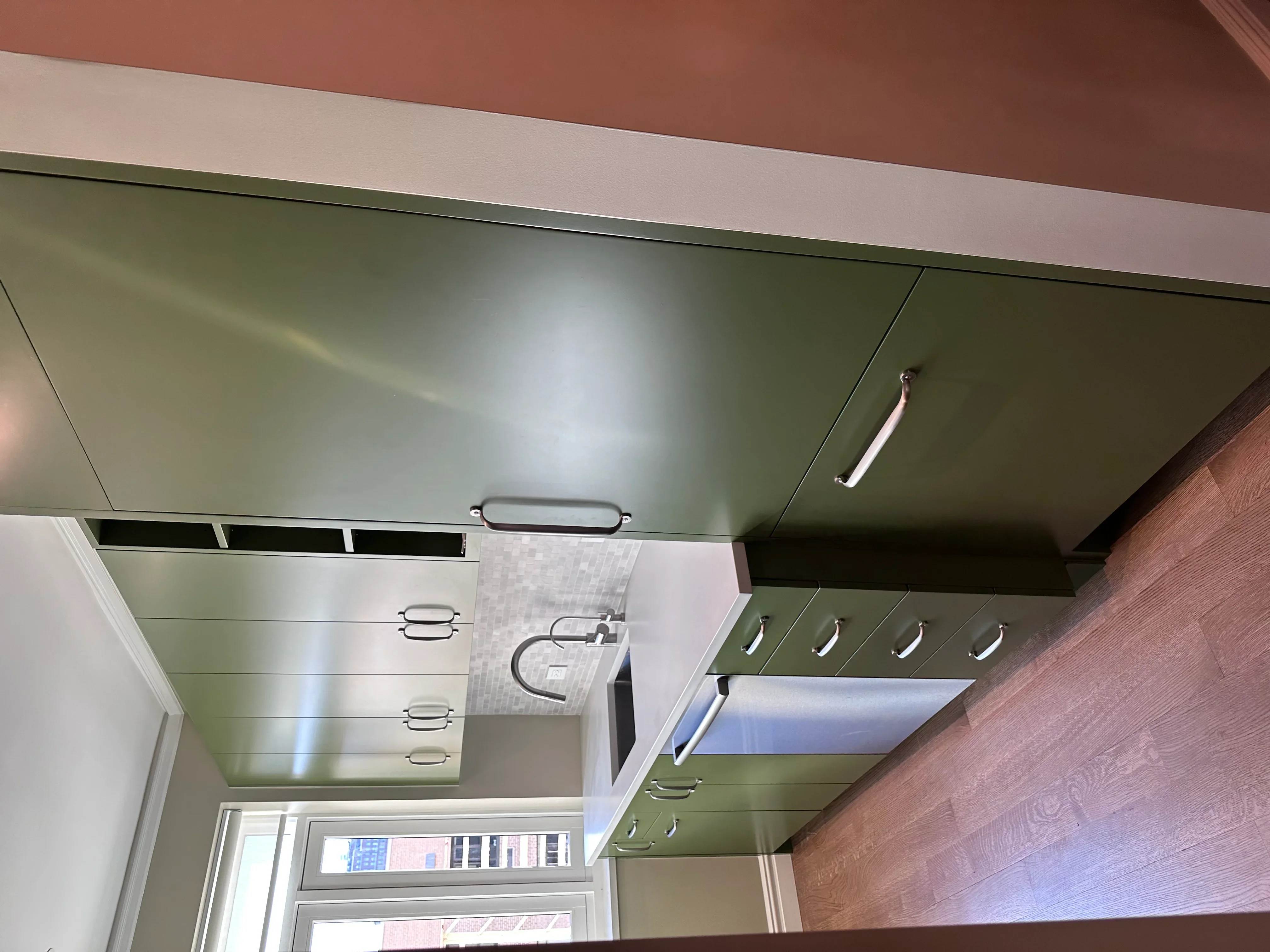 Sage green kitchen cabinets with chrome handles and recessed lighting installed in modern kitchen