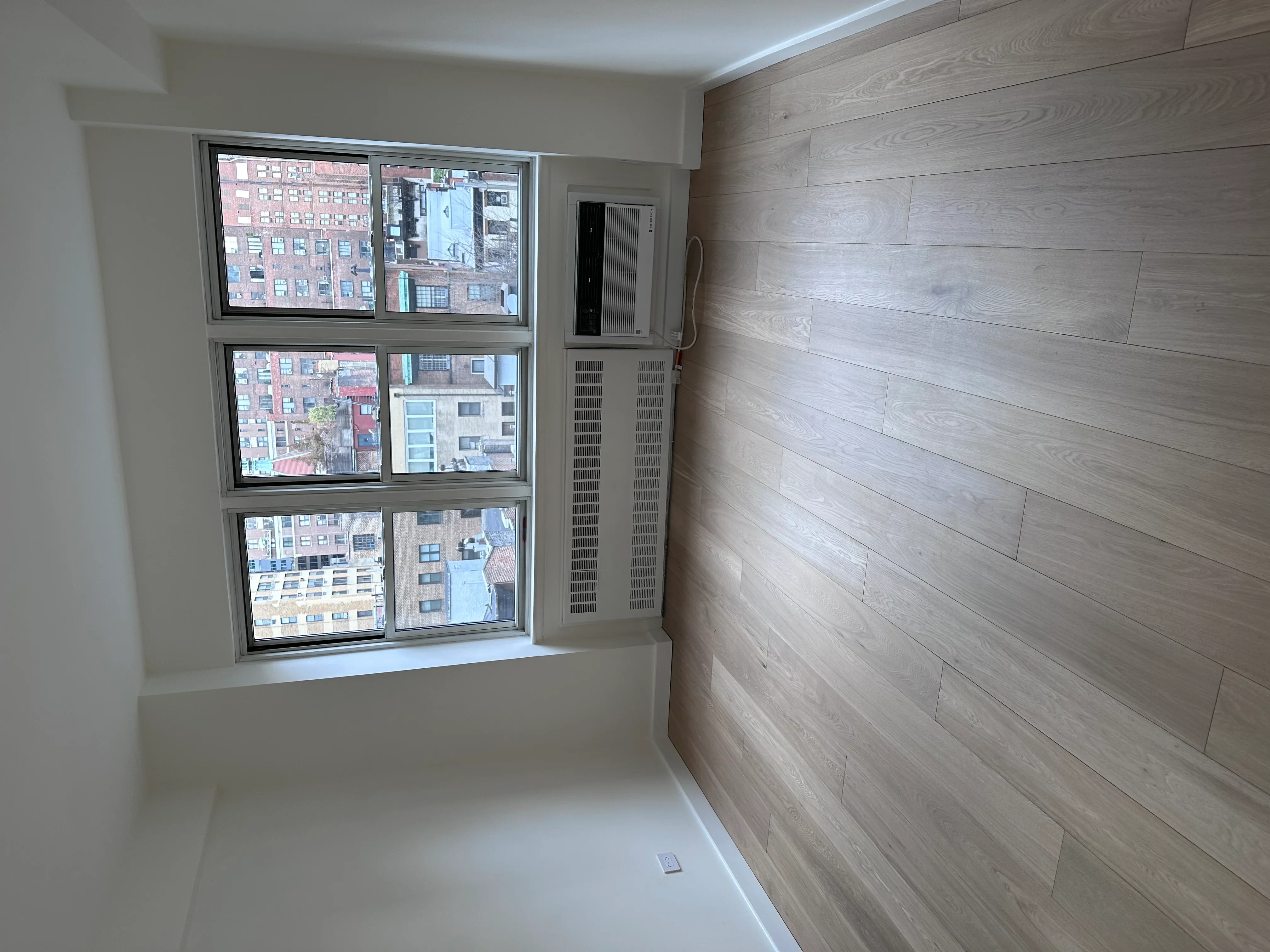Modern room with horizontal wood accent wall and three-panel aluminum-framed windows overlooking urban buildings