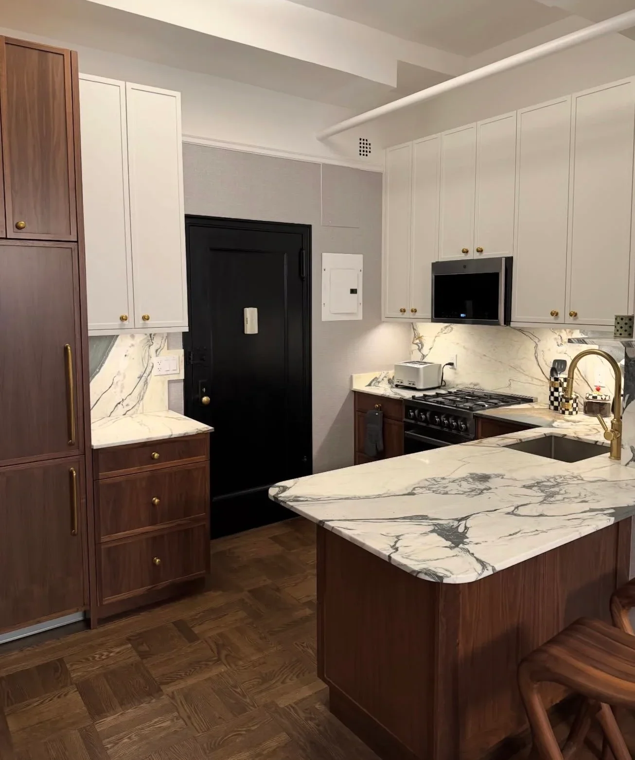 Modern kitchen with cream and walnut cabinetry, marble counters, and gas range
