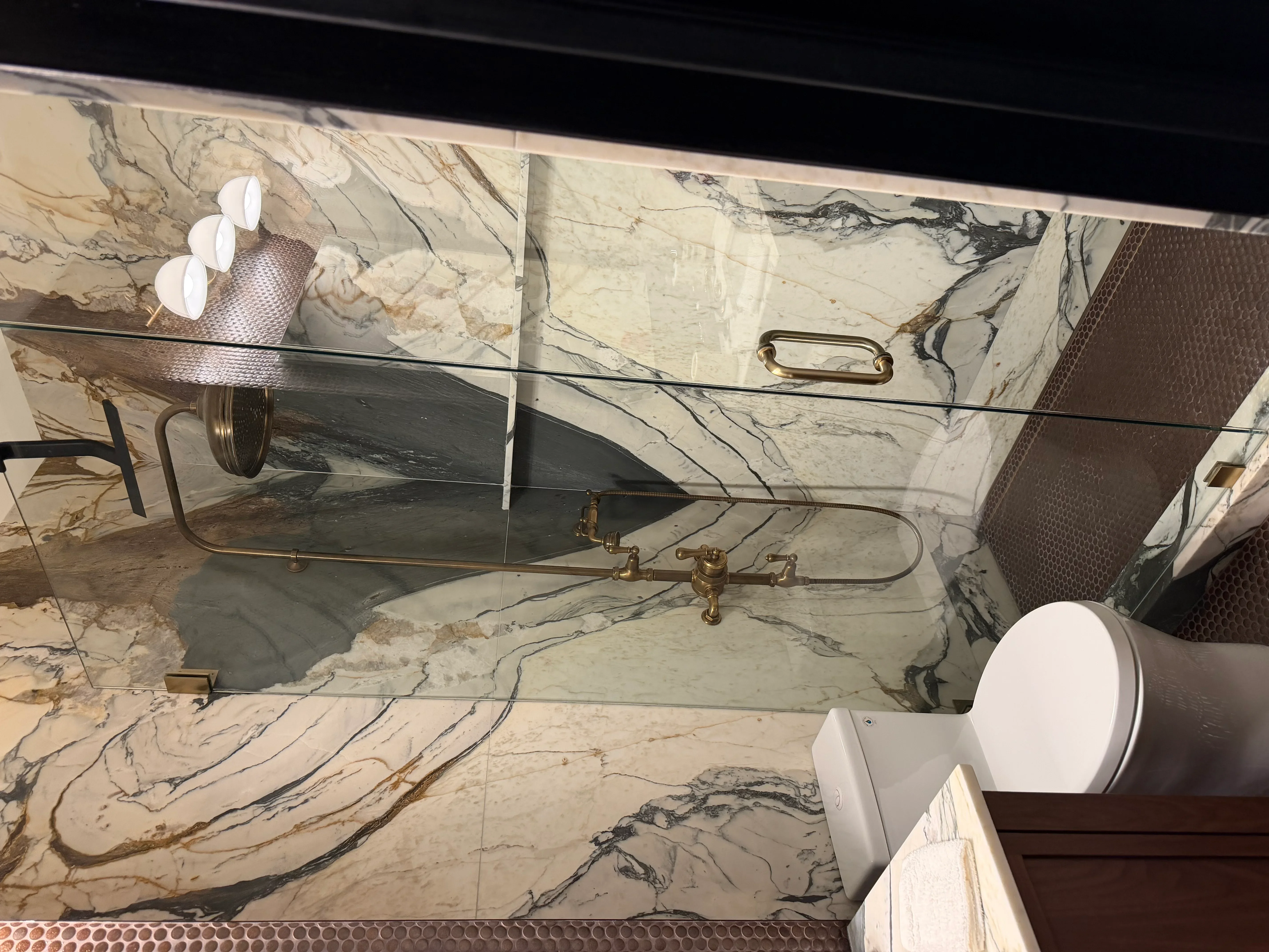 Marble bathroom vanity with glass mirror, brass fixtures, and white lighting sconces