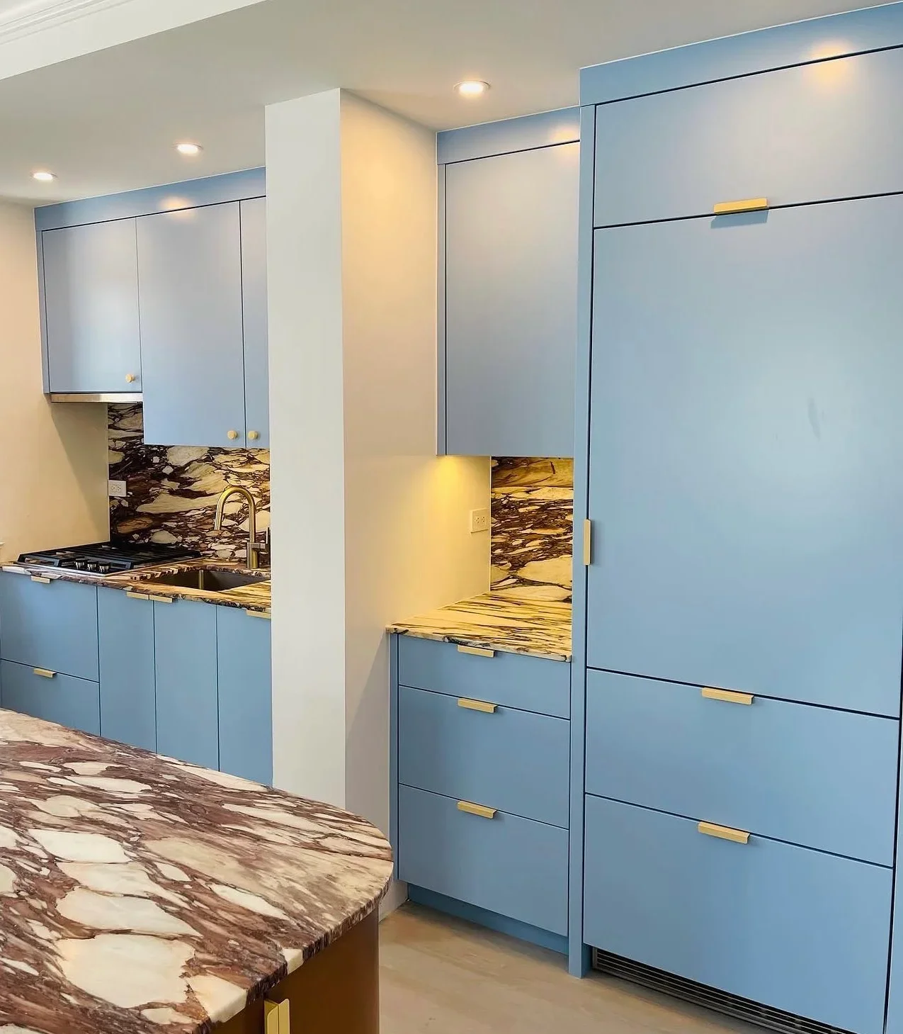 Modern kitchen with blue cabinetry, marble countertops, and brass hardware