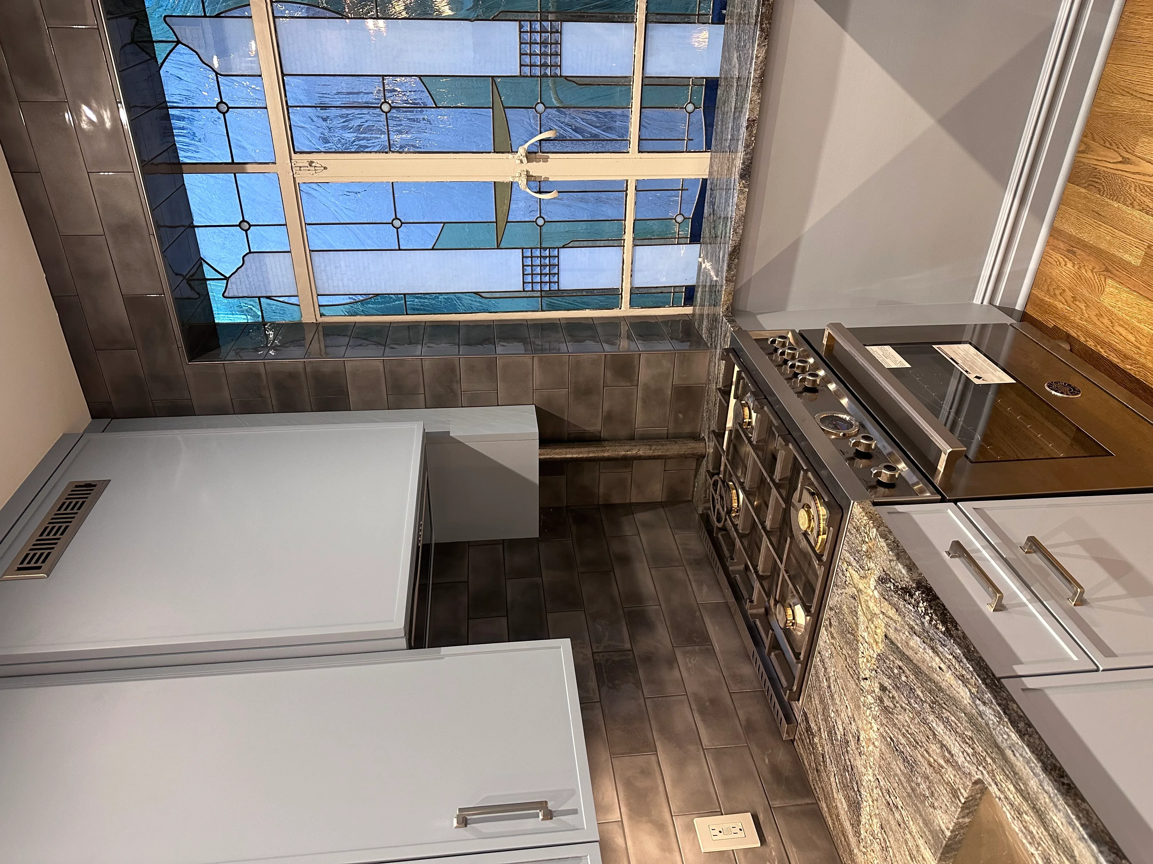Modern kitchen with stained glass window, gray tile floor, and stainless steel range