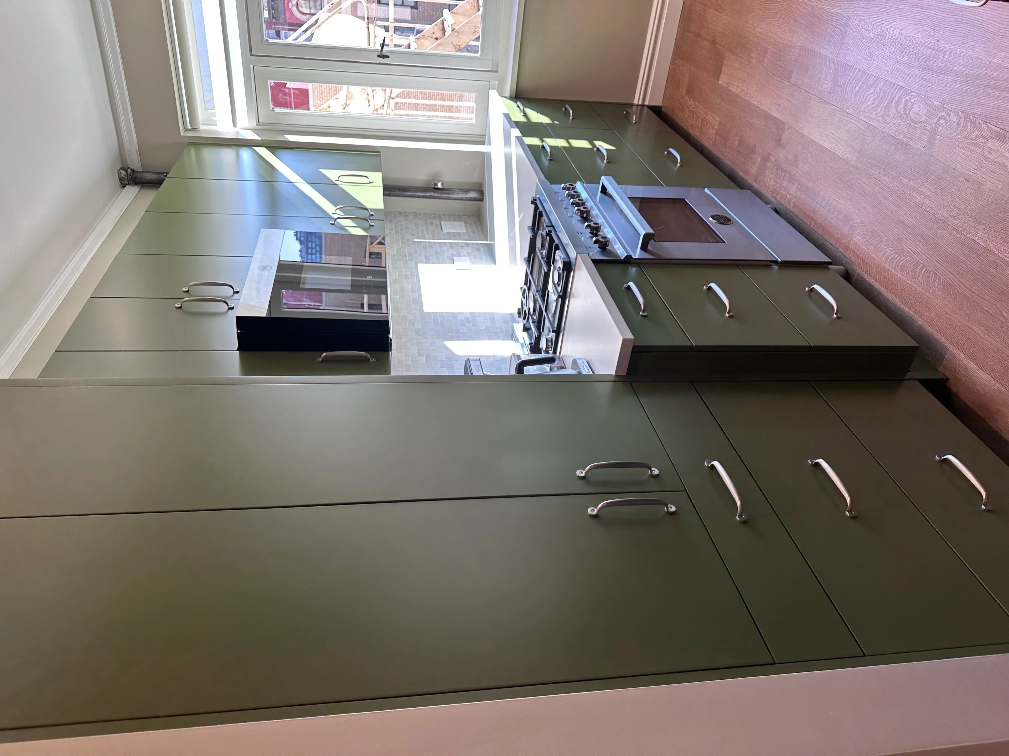 Modern kitchen with olive-green cabinets, gas range, and city view windows