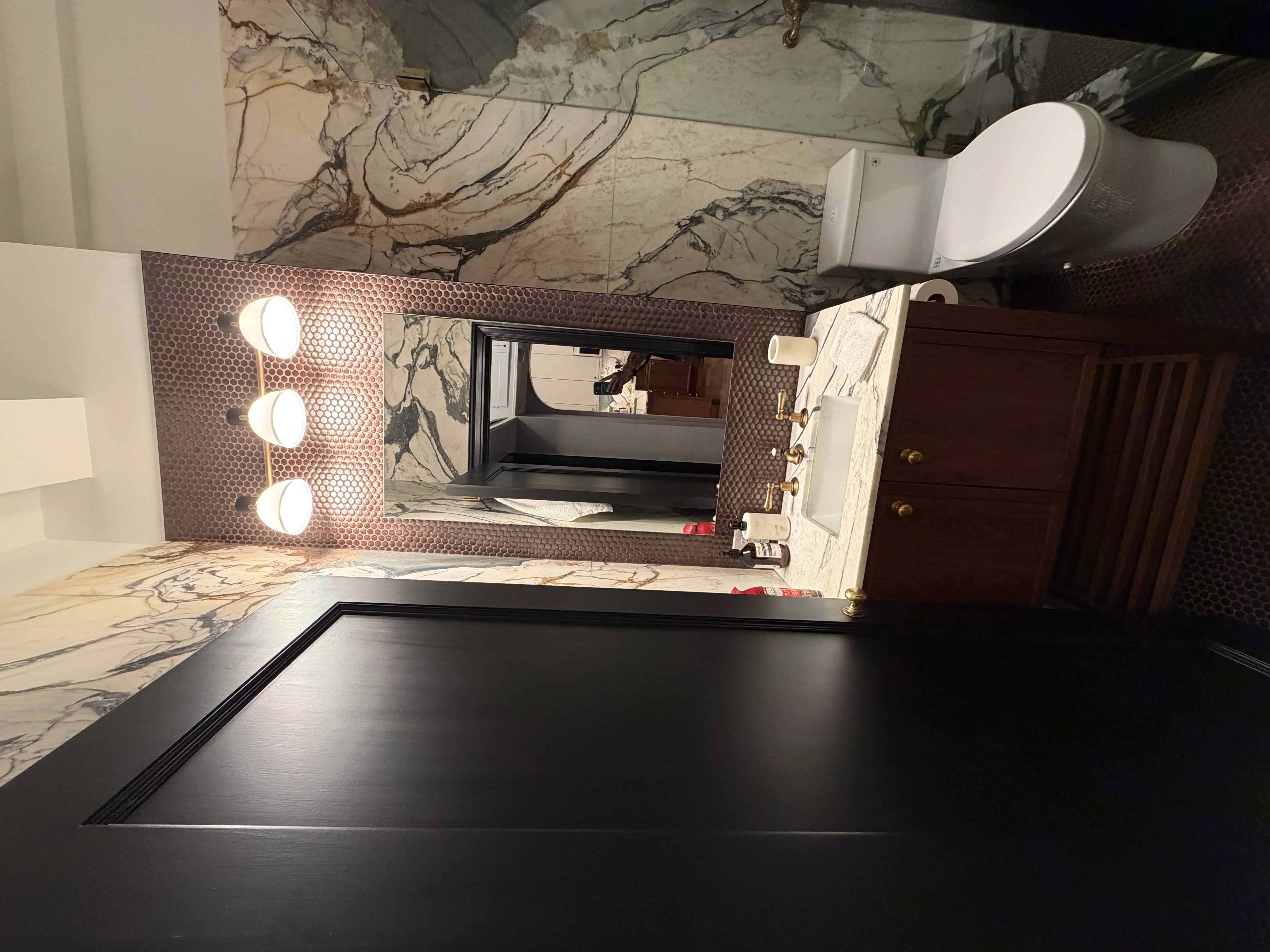 Bathroom vanity with marble countertop, three-bulb lighting fixture, and framed mirror