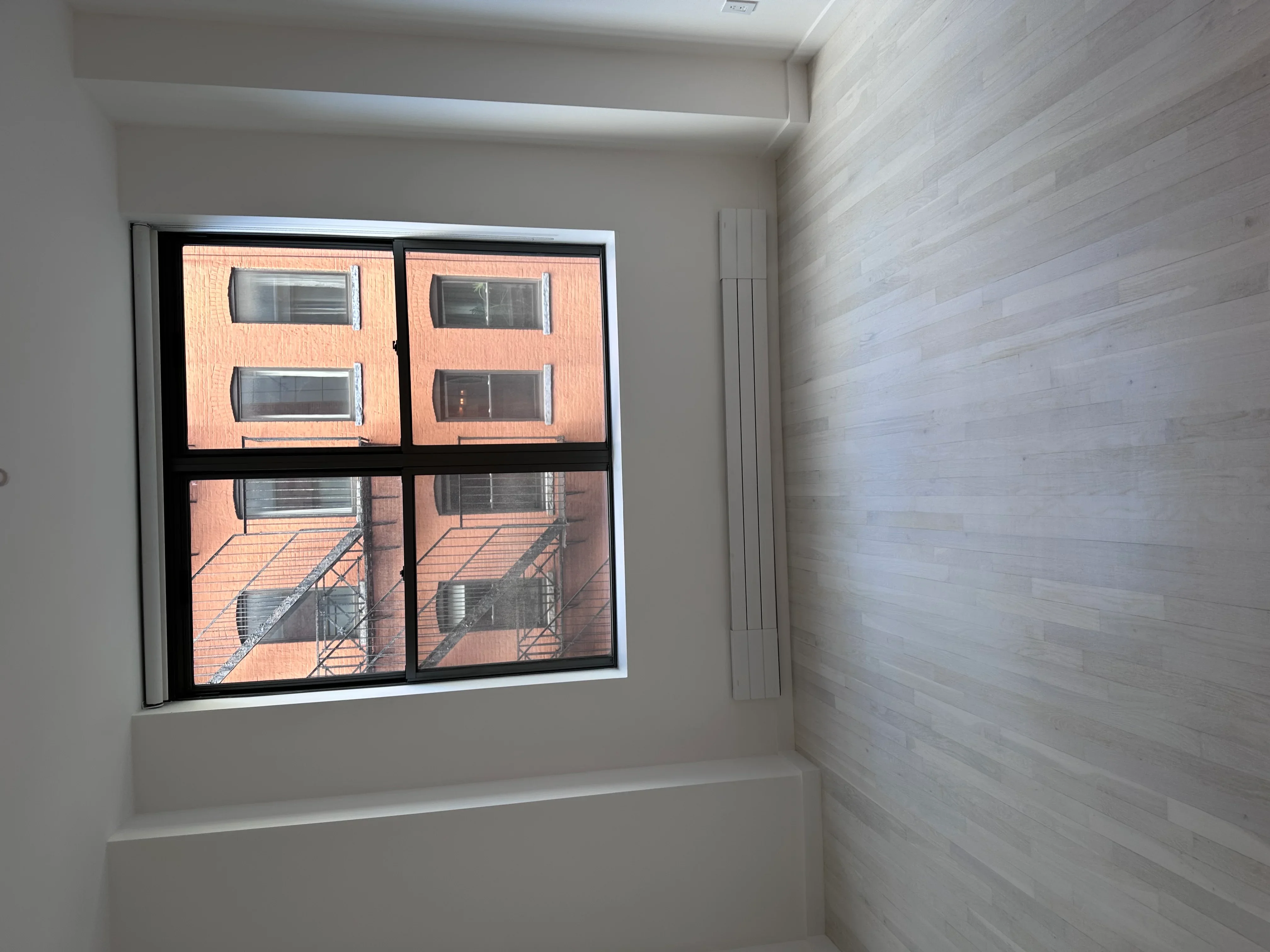 Four-pane black-framed window installed in white drywall with light wood accent wall