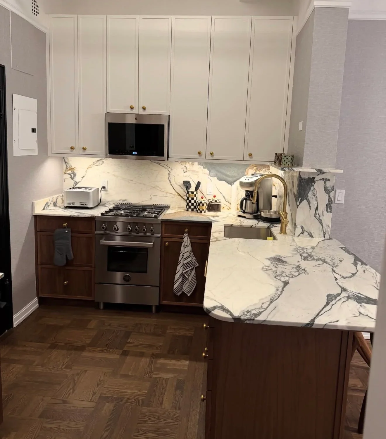 Modern kitchen with cream and dark wood cabinetry, marble countertops, and stainless steel appliances