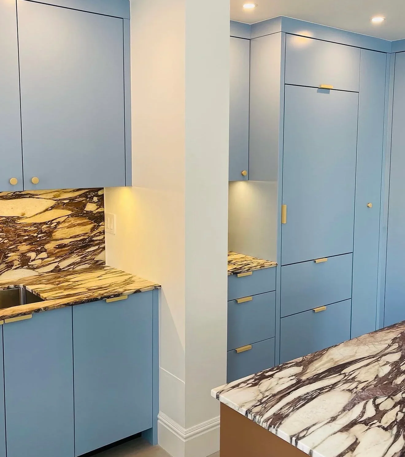 Blue kitchen cabinets with marble countertops and brass hardware in modern kitchen