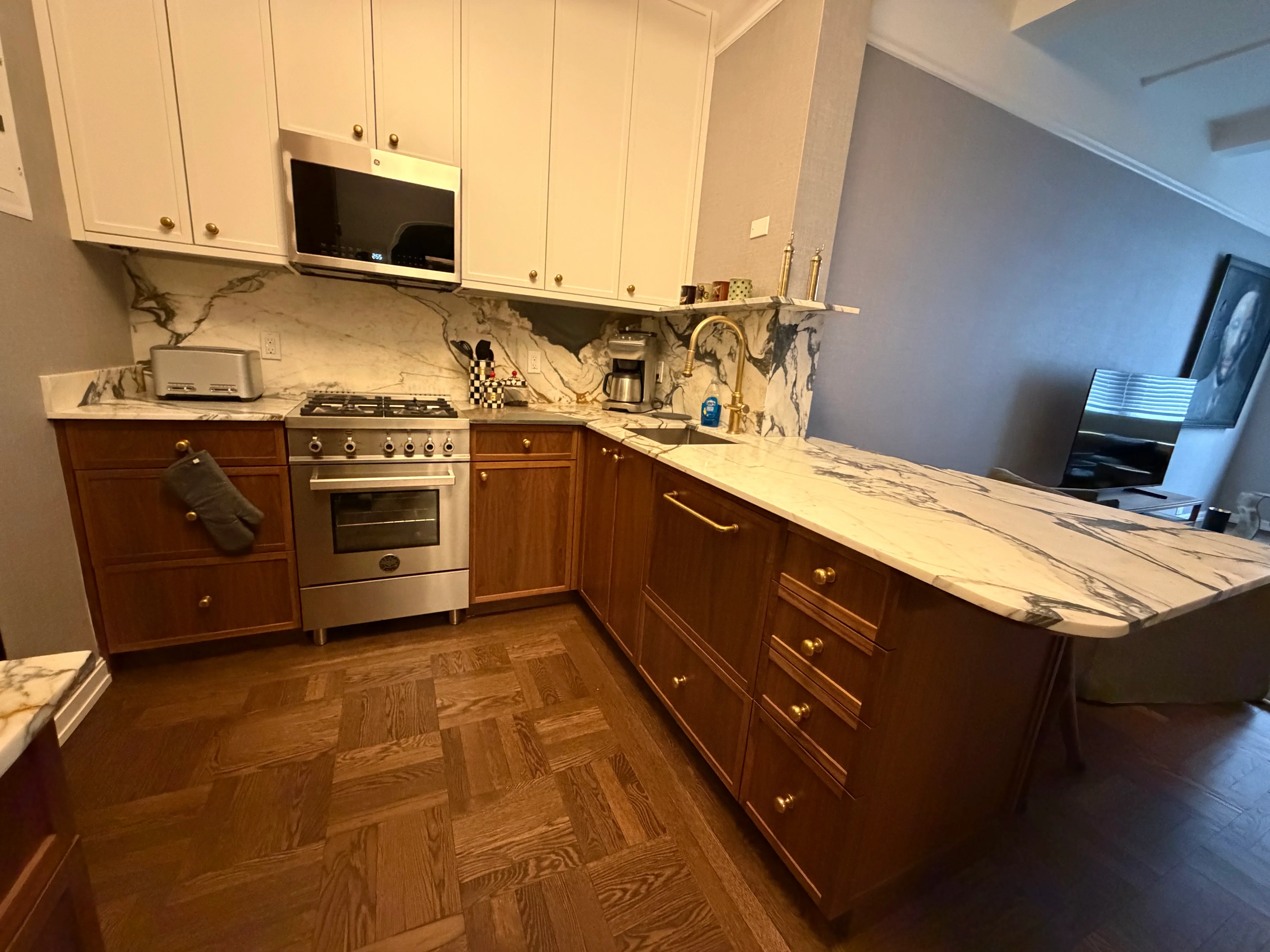 Kitchen with cream and wood cabinets, marble counters, stainless steel range, and herringbone wood floor