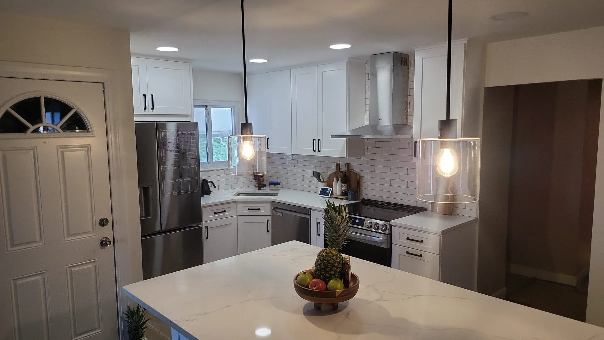 Modern kitchen with white cabinets, marble island, stainless steel appliances, and pendant lights