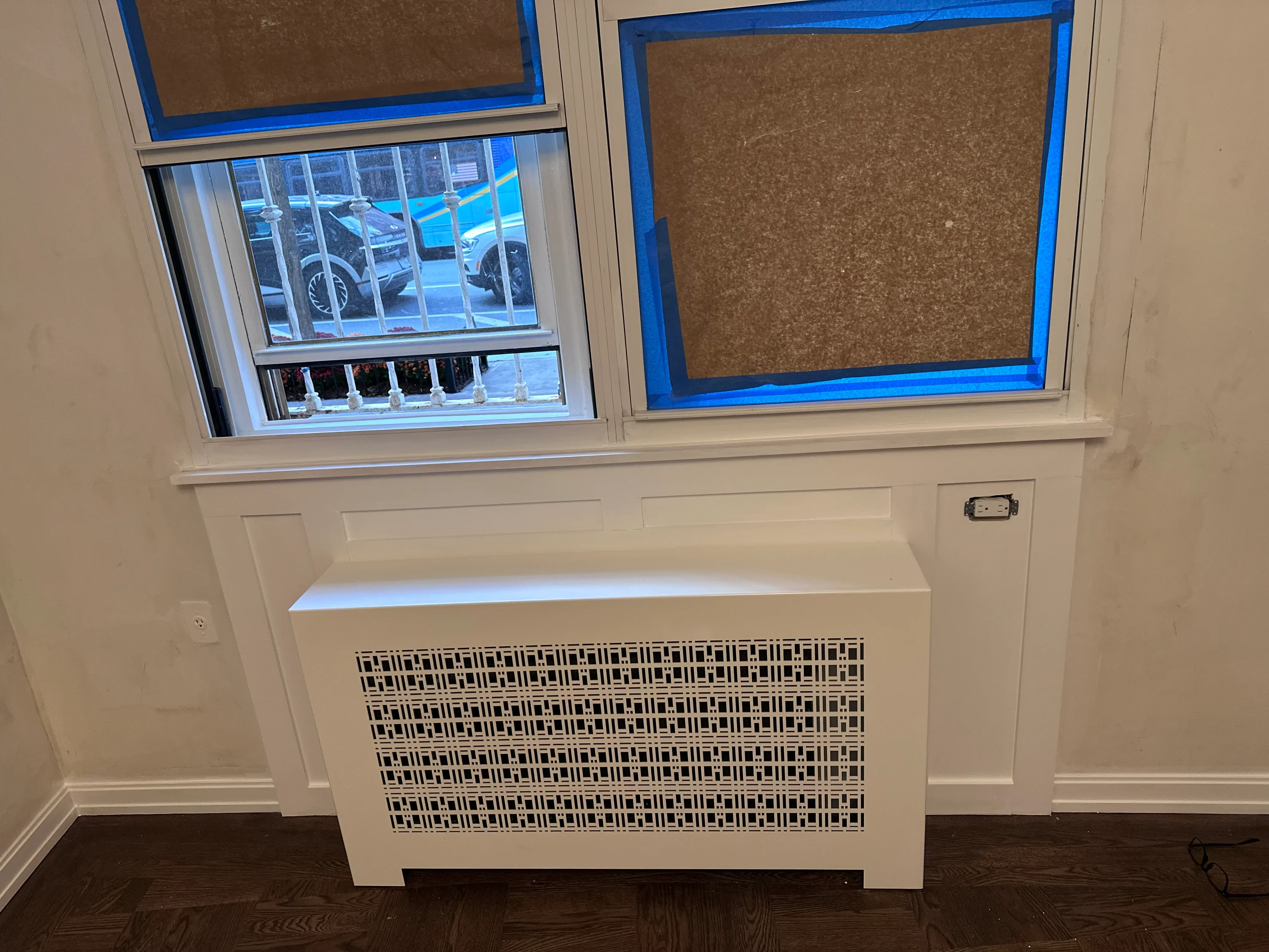 Cream-painted window seat with built-in radiator cover and cork bulletin boards above