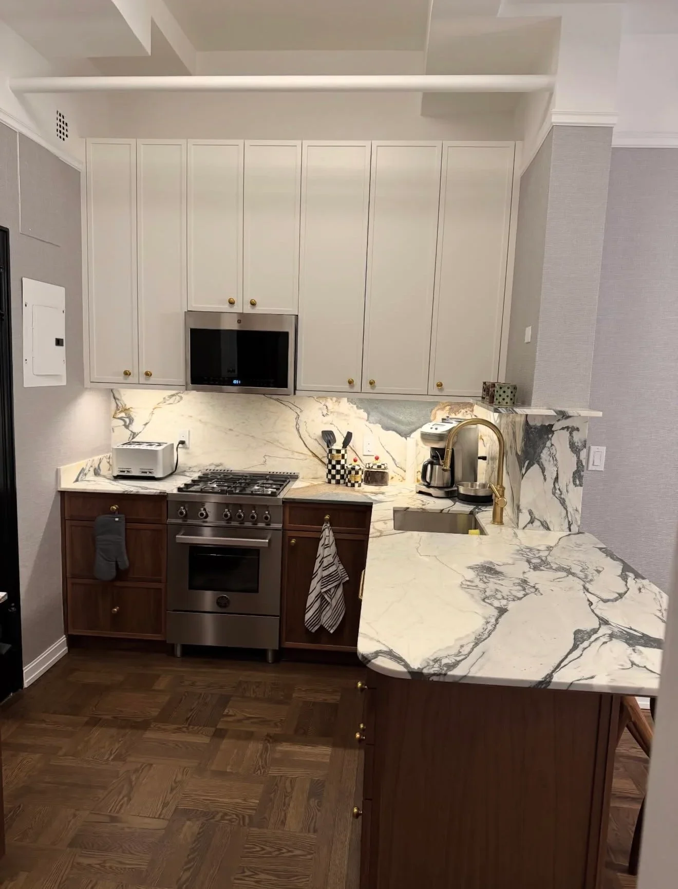 Modern kitchen with cream and dark wood cabinetry, marble countertops, and stainless steel appliances